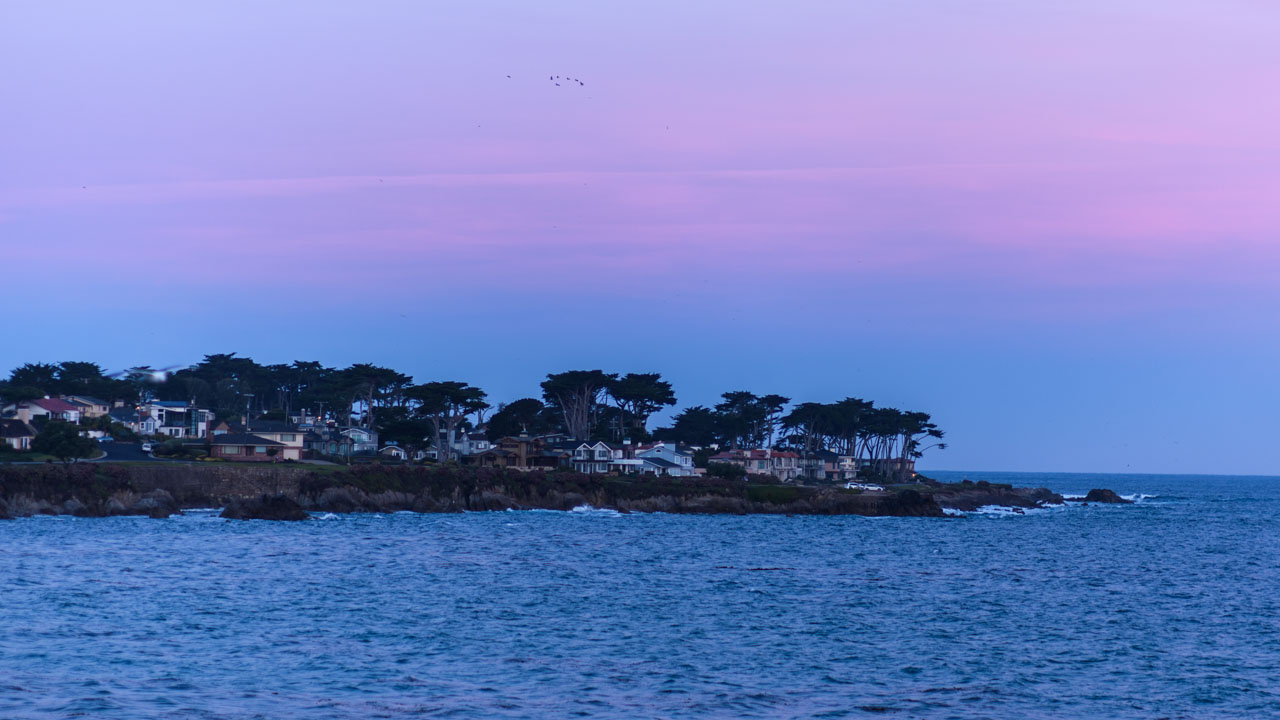 Coastal houses and sea seen from Lovers Point Park in Monterey before dawn under a pink sky